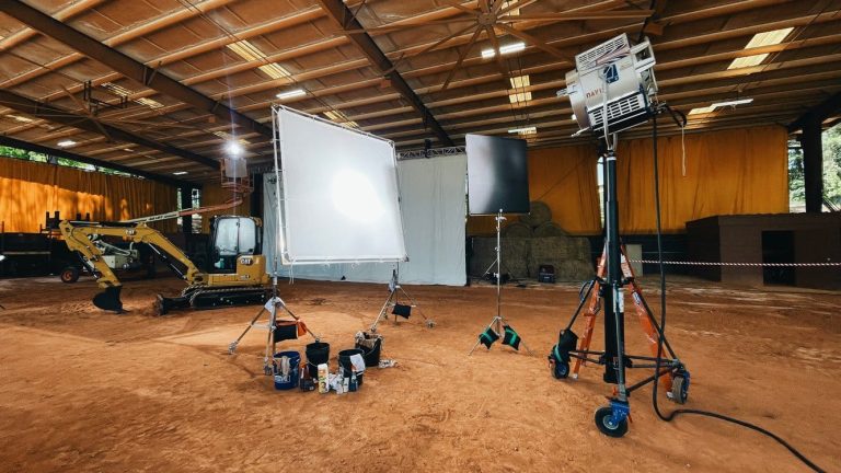 Caterpillar excavator on a film set with studio lighting equipment in a large indoor facility, capturing industrial scenes for production.