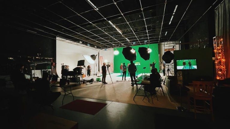 A behind-the-scenes view of a Caterpillar production set in a large studio with a green screen, lighting equipment, and crew members preparing for filming.