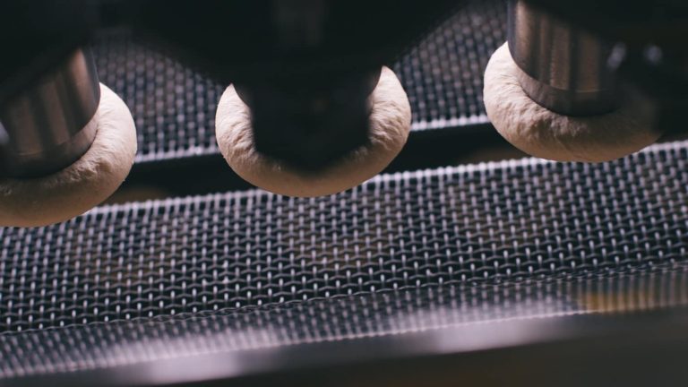 Krispy Kreme dough undergoing shaping on a production line, showing the precision machinery used in the donut-making process.