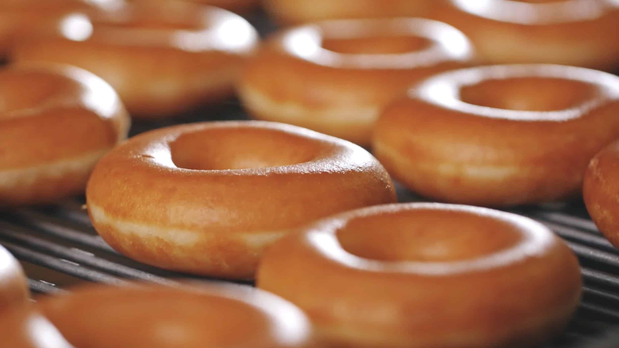 A close-up view of freshly baked glazed Krispy Kreme doughnuts on a conveyor belt.