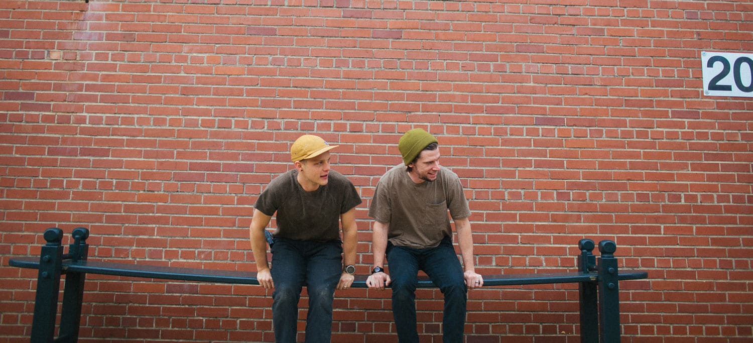 Two crew members from the South State Bank commercial sit casually on a metal rail against a brick wall, sharing a light moment during the shoot.
