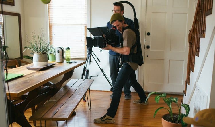A camera crew captures a scene inside a home during the production of the South State Bank commercial, with a cameraman focused on filming a dining area.