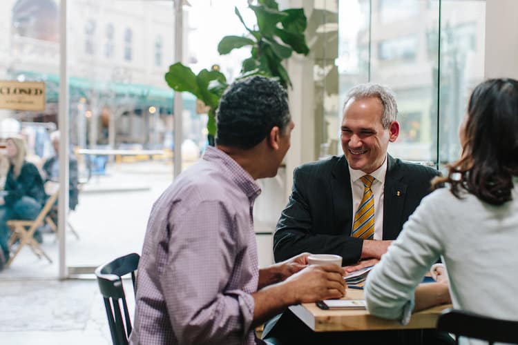 A South State Bank representative in a suit shares a conversation with two customers over coffee in a bright café, highlighting the bank’s commitment to personalized financial services and community engagement.